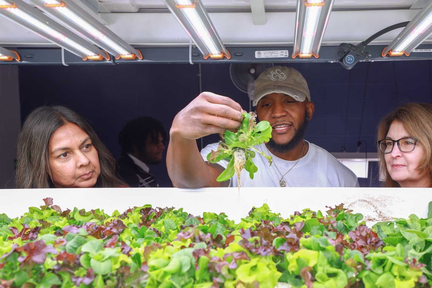 Desmond Hayes holding freshly grown greens beside visitors and a hydroponic growing bed at iA Labs